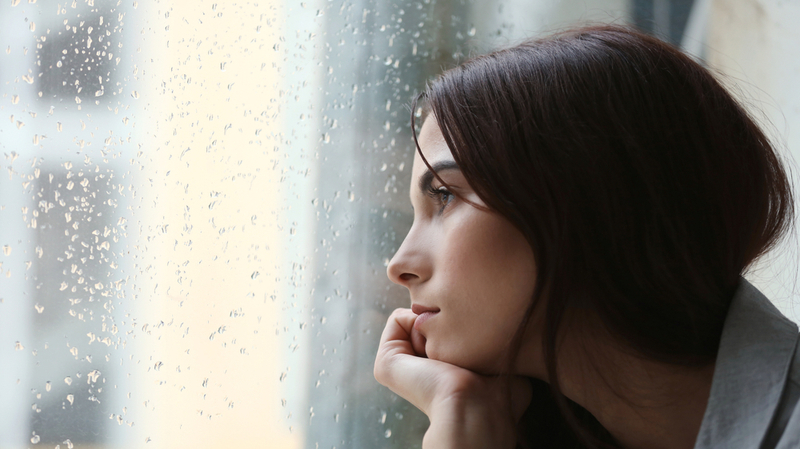 雨降りの景色を窓から見ている女性